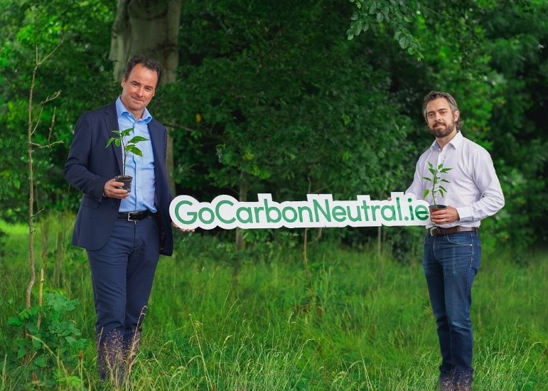 An image of Ocuco CEO, Leo Mac Canna, and a man holding tree saplings and a "GoCarbonNeutral.ie" sign in an outdoor setting.