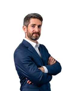 A photo of Patrick Broe. Patrick has dark hair and a beard, wearing a navy suit and a white shirt.