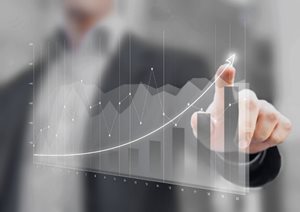 The image shows a man pointing at a projected graph of financial data. The graph shows a positive trend, with a line curving upwards and bars increasing in height