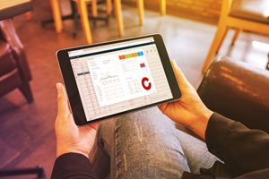 An image of a person holding a tablet. On the screen are different reports and graphs.