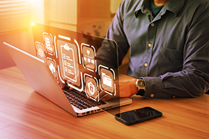 An image of a person using a laptop. Overlaid on the image are white icons that include a folder, a lock and a clipboard.