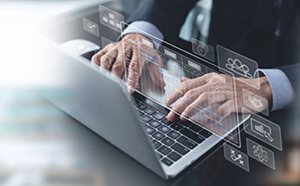 The image shows a person sitting at a desk and working on a laptop computer. Over the top of the laptop screen are computer icons, suggesting the person is working with data and applications.